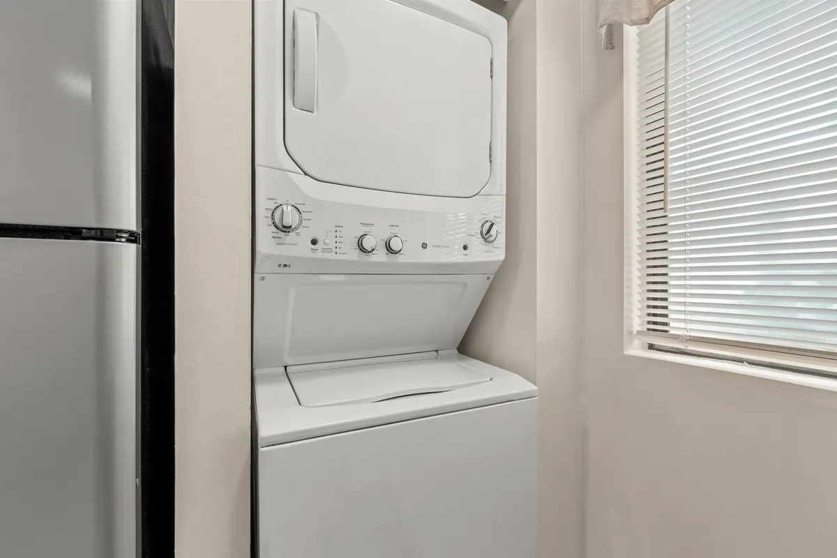 A practical laundry area featuring an in-unit washer and dryer next to a bright window with blinds. The area is tidy and functional, providing convenience for guests and families.