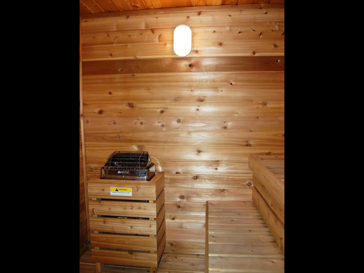 A warmly lit sauna interior with wooden benches and walls, featuring a sauna heater and a cozy, tranquil atmosphere—perfect for relaxing after a night out or bonding with friends over wellness routines.