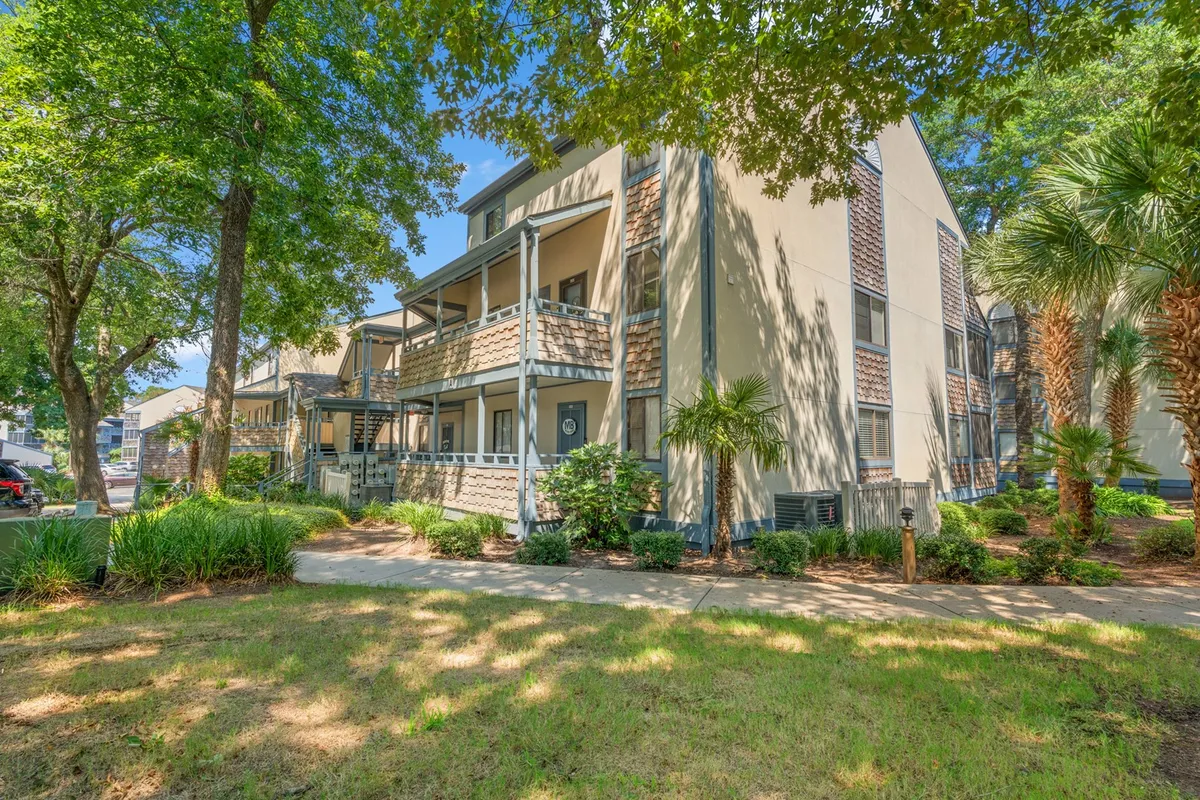 This image displays the exterior of Summertree Village, with mature trees, inviting balconies, and the building's welcoming facade. People can be seen enjoying a walk and gathering outdoors, set against a backdrop of lush greenery, highlighting the tranquil neighborhood setting.