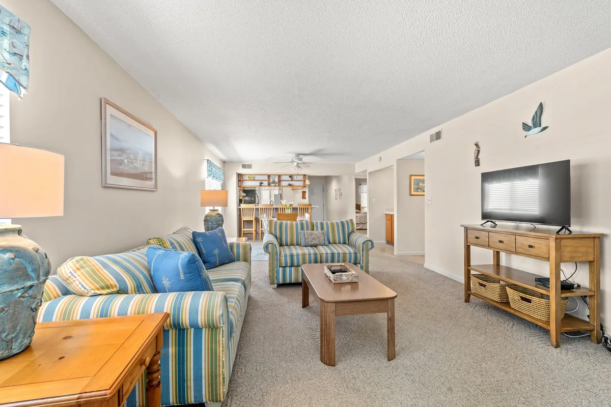 A closer look at the living area highlights a plush striped sofa, a wooden coffee table perfect for group activities, a TV unit for movie nights, and a decorative lamp that adds a warm, inviting glow. The arrangement invites guests to unwind and share meaningful moments together.