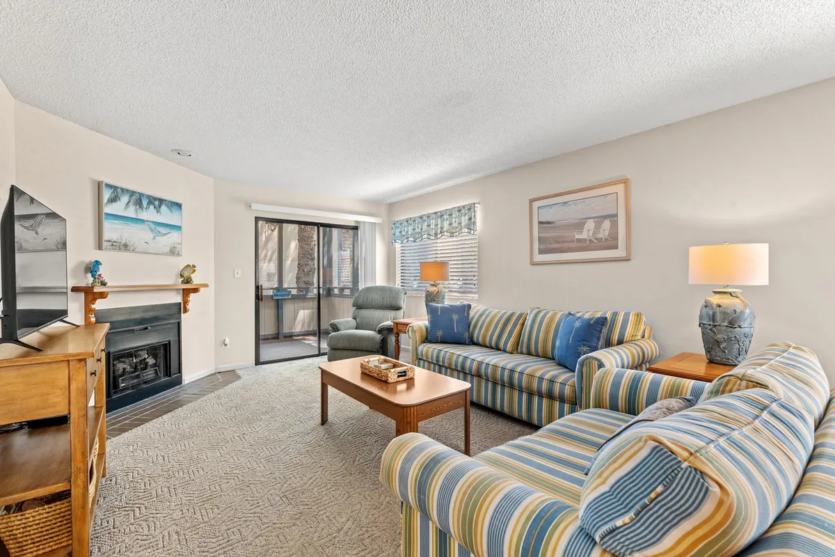 This image showcases a welcoming living area with striped sofas arranged around a fireplace, a large window that fills the space with natural light, and decorative artwork that adds a personal touch. The area exudes comfort and is designed for both relaxation and social gatherings, making it ideal for family or group activities.