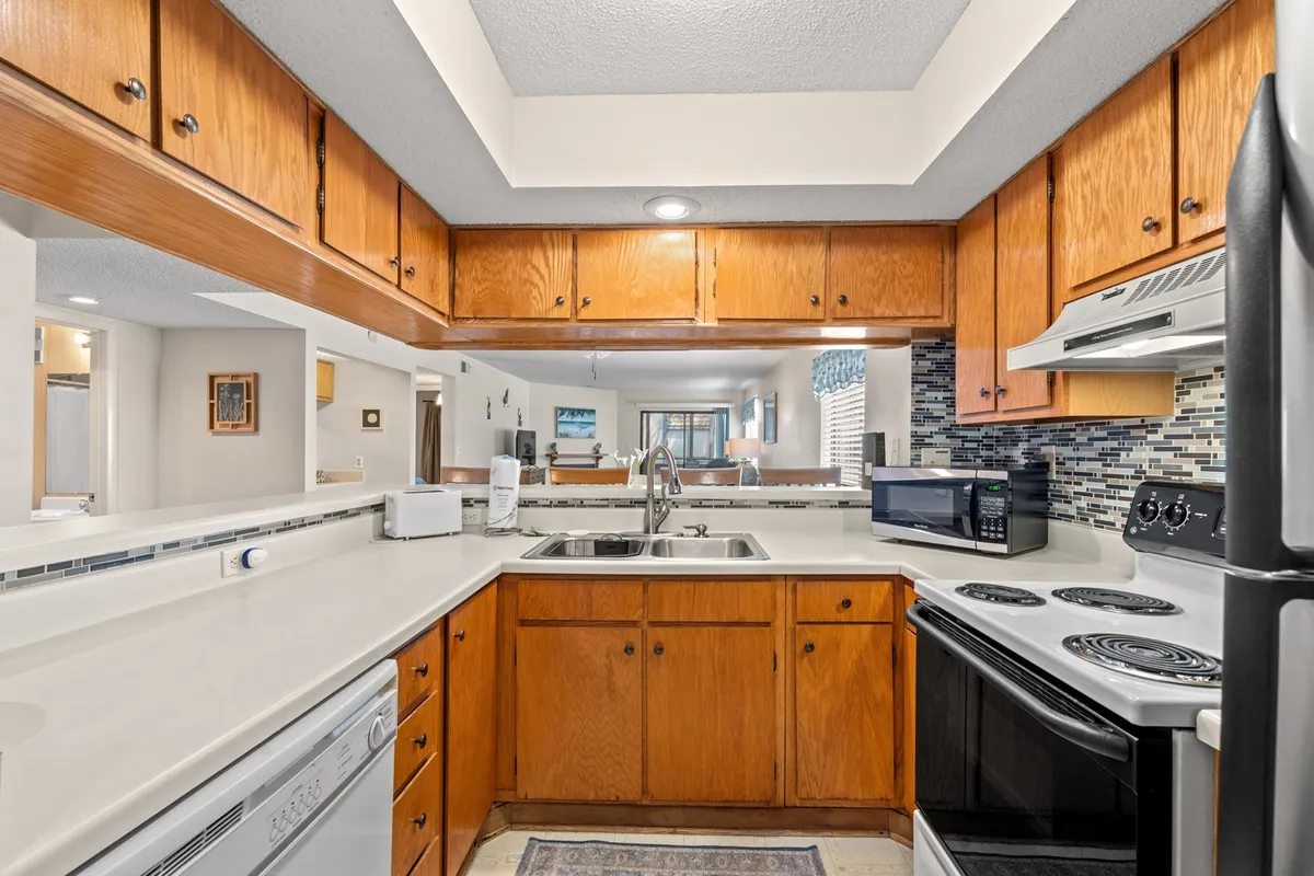 A view of the kitchen featuring cabinetry, countertop, sink, and visible appliances. Sunlight streams into the space, highlighting a warm and inviting atmosphere ideal for morning breakfasts or family gatherings.