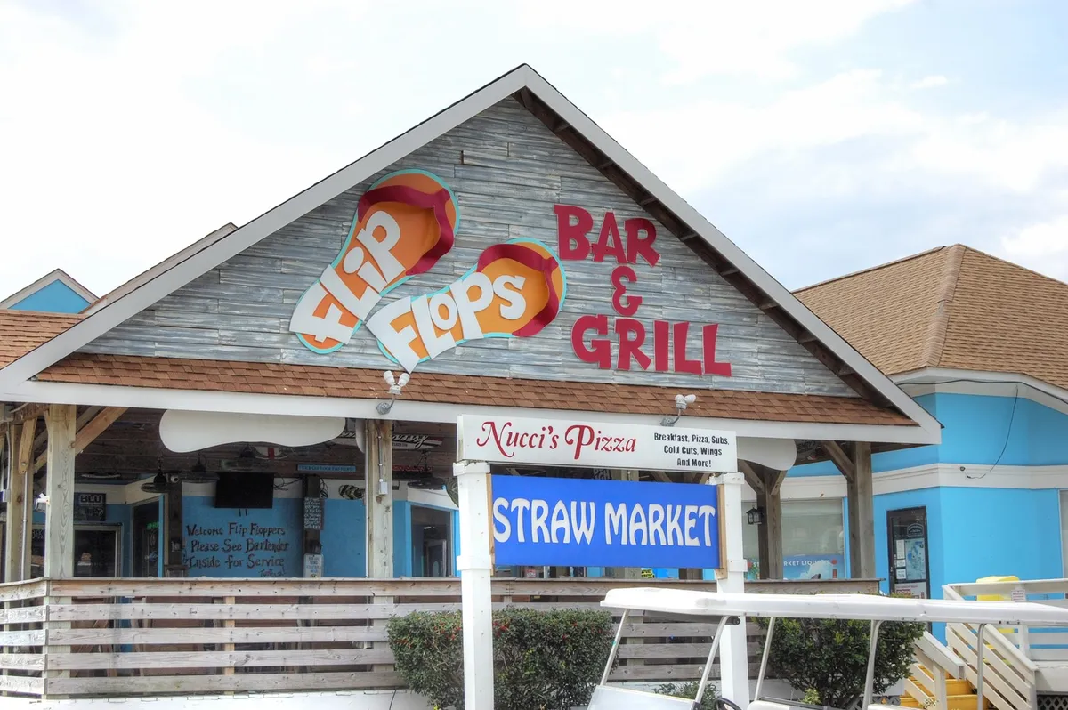 This exterior image features the welcoming signs for Flip Flops Bar & Grill, Straw Market, and Nucci's Pizza, all set amidst an inviting outdoor setting. The area appears relaxed, ideal for groups to gather before heading out for a night on the town or settling in for casual drinks and dining.