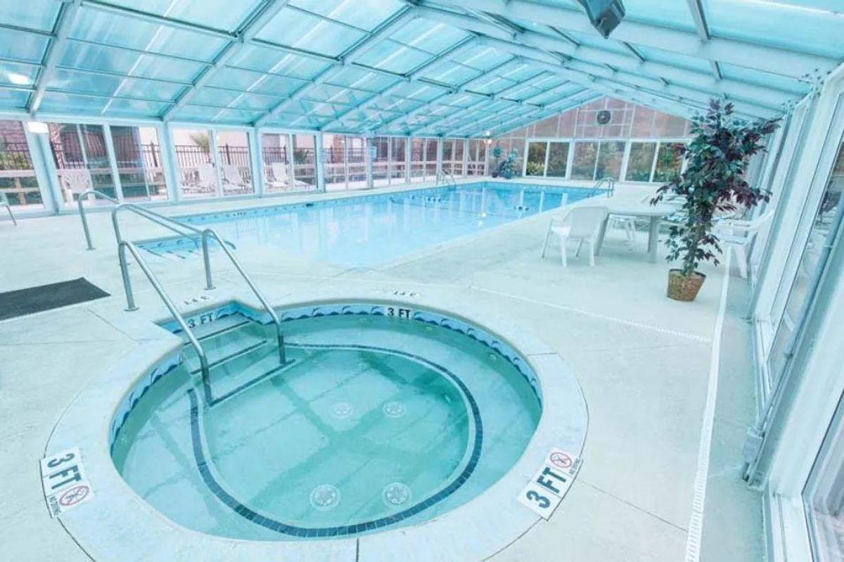 A spacious indoor pool area with a sparkling swimming pool, a jacuzzi, and comfortable seating around the perimeter. The atmosphere is tranquil and inviting, suitable for morning swims or relaxing social gatherings.
