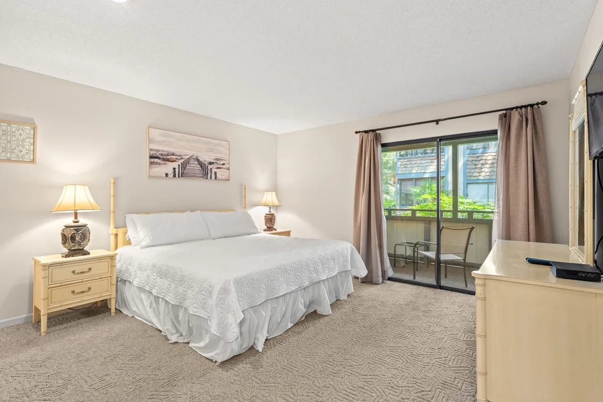 This image features a serene bedroom with a comfortable bed, nightstands, a sliding glass door letting in natural light, and tasteful artwork. The ambiance is calm and restful, ideal for a private sanctuary after an active day.